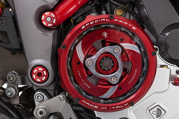 Close-up view of a red anodised clutch cover with transparent disc. Behind it is a red-silver anodised pressure plate and a silver anodised spring plate. 