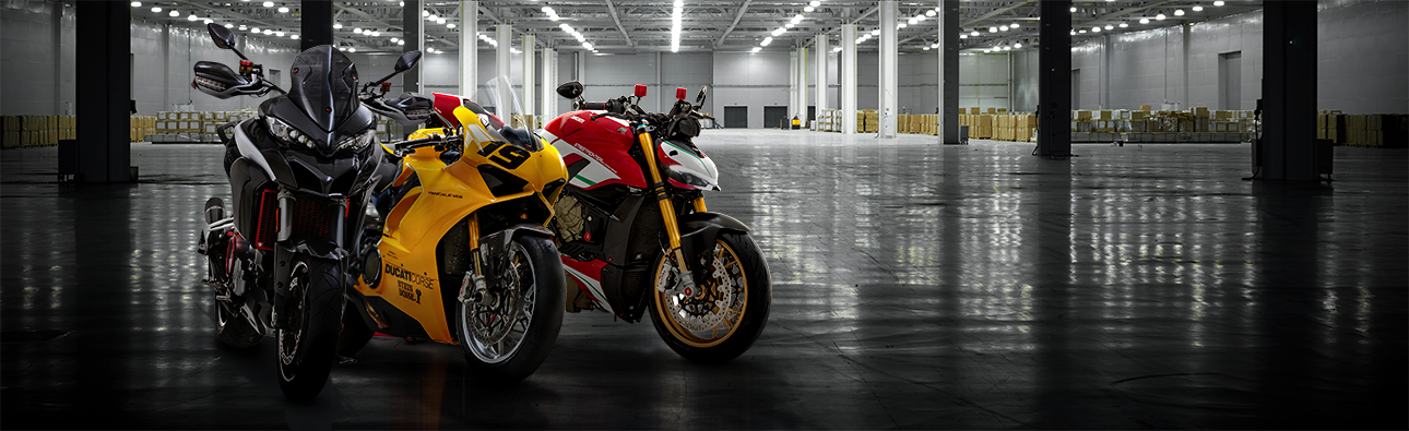 Une Ducati Multistrada noire, une Ducati Panigale jaune et une Ducati Streetfighter rouge se trouvent dans un entrepôt.