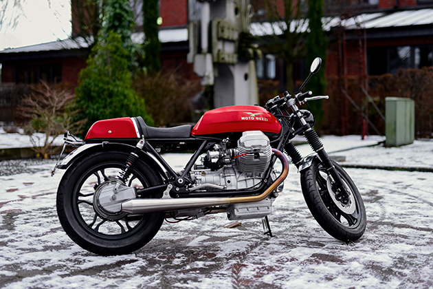 You can see a red petrol tank with the Moto Guzzi logo, two silver wheel rims, a silver V2 engine block and various frame and suspension parts.