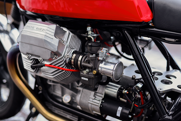 Several freshly restored Moto Guzzi engine parts are lying on a workbench. The parts include cylinder heads, cylinder blocks, valve covers and other components in perfect condition.