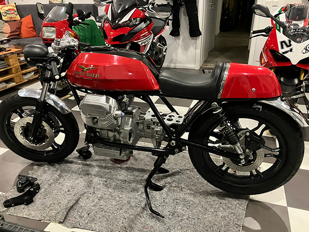 Dismantled red Moto Guzzi with a workshop in the background. Various tools and care products can be seen around it.